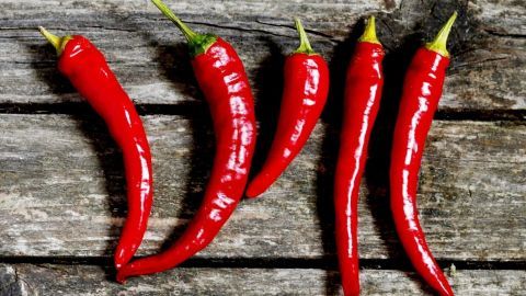 Leuchtend rote Chilischoten liegen auf einem rustikalen Holzuntergrund, bereit zur Verwendung gegen Rückenschmerzen.
