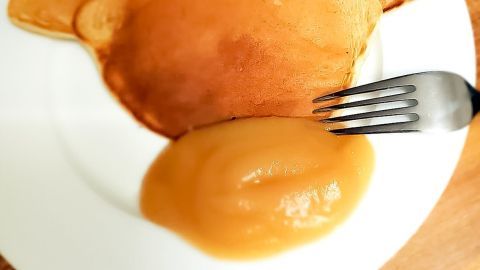 Ein Teller mit drei Pfannkuchen, auf dem eine Portion selbstgemachtes Apfelmus serviert wird, mit einer Gabel daneben.