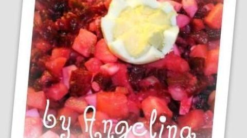 Ein bunter Roter Kartoffelsalat ist in einer Schüssel angerichtet, mit einem Ei als Dekoration in der Mitte. "by Angelina" steht unterhalb.