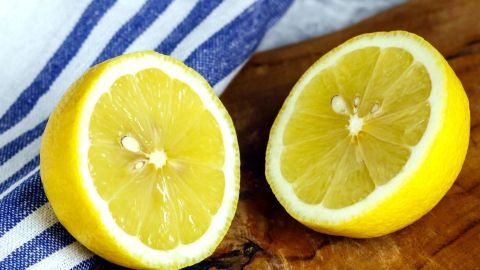 Zwei halbierte Zitronen liegen auf einem Holzbrett, umgeben von einem blauen und weißen Geschirrtuch.