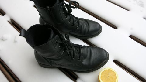Schwarze Stiefel stehen auf schneebedecktem Holz. Daneben liegt eine halbe Zitrone als Hausmittel gegen Schneeränder.