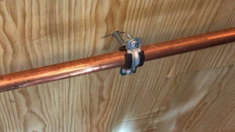 Ein Heizungsrohr ist an einer Holzvertäfelung befestigt und zeigt eine hochwertige Verbindung, die in modernen Wohnräumen eingesetzt wird.