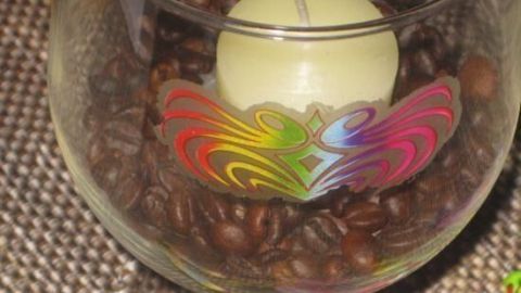 Ein Glas mit Kaffeebohnen und einer Kerze darin steht auf einem Tisch, dekoriert mit bunten Farben.