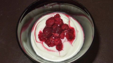 Ein Dessert aus cremigem Joghurt mit frischen Himbeeren obendrauf, serviert in einer eleganten Schüssel auf einem dunklen Untergrund.
