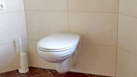 Eine weiße Toilette steht in einem hell gefliesten Raum, bereit für die Entkalkung mit Waschmaschinenentkalker.