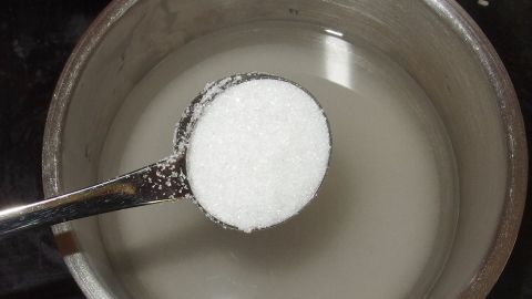 Ein Löffel Zucker wird in eine Schüssel mit Wasser gegeben, um Läuterzucker herzustellen.