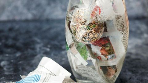 Ein Glasgefäß ist mit zerknülltem Zeitungspapier gefüllt, das zum Reinigen der Blumenvasen verwendet wird, auf einer dunklen Oberfläche.