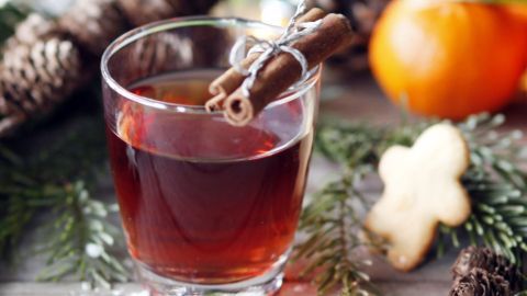 Ein Glas Glühwein-Sangria steht auf einem Tisch, umgeben von Tannenzweigen, einer Orange und einem Plätzchen.