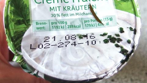Deckel von Joghurtbechern und dergleichen können beim Zahlen an der Kasse schnell kaputt gehen, wenn die Fingernägel zu lang sind. Ein Hand hält einen Becher Crème Fraîche mit Kräutern, das Haltbarkeitsdatum zeigt den 21.08.16 an.