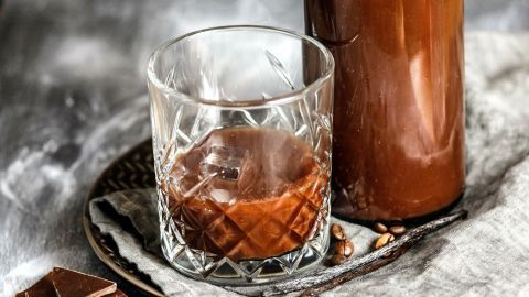 Eine Flasche selbstgemachter Schokoladenlikör steht neben einem Glas mit dem Likör auf einem rustikalen Teller.