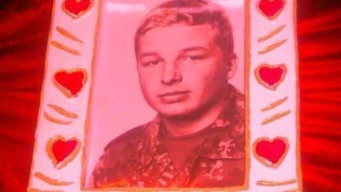 Ein Bilderrahmen aus Styropor, geschmückt mit roten Herzen, hält ein Porträt eines jungen Mannes im Militäruniform.