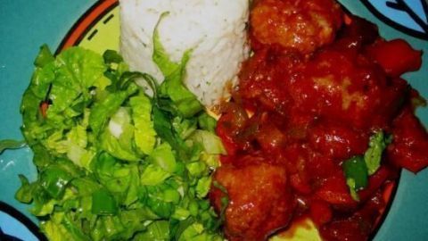 Zigeunerklößchen sind auf einem bunten Teller mit Reis, scharfer Sauce und frischem Salat angerichtet.
