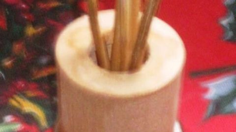 Ein Duftdiffuser mit Holzstäbchen steht auf einer roten Tischdecke mit Weihnachtsmotiv.