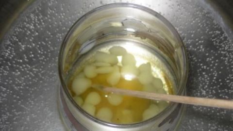 Ein Glas mit geschmolzenem Lippenbalsam und Honig wird mit einem Holzstäbchen im Wasserbad gerührt.