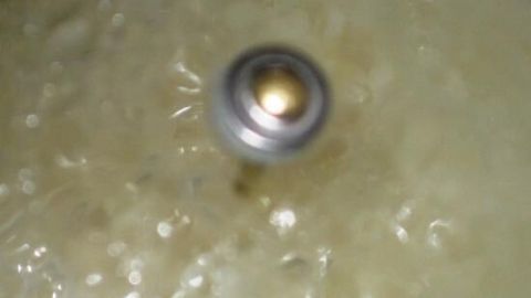 Ein Topfdeckelventil verschließt das Dampfloch, während kochendes Wasser darunter brodelt und Blasen wirft.
