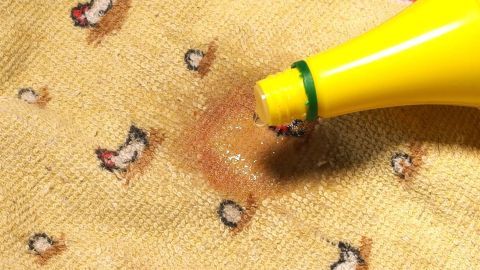 Ein Gel-Stift wird auf einen gelben Stoff mit Obstflecken aufgetragen, um die Flecken zu entfernen.