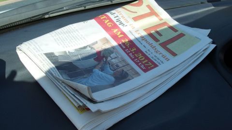 Eine dicke Zeitung liegt auf dem Armaturenbrett eines Autos, während die Sonne durch die Frontscheibe scheint.