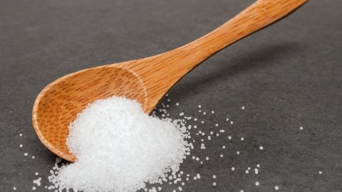 Ein Holzlöffel hält Kochsalz, das auf einer dunklen Oberfläche verstreut ist, bereit zum Entfernen von Kaugummiflecken aus Jeans.