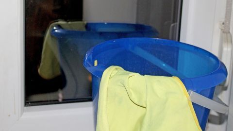 Ein blauer Mülleimer steht neben einem Fensterrahmen, während ein gelbes Tuch auf den Eimer gelegt ist.