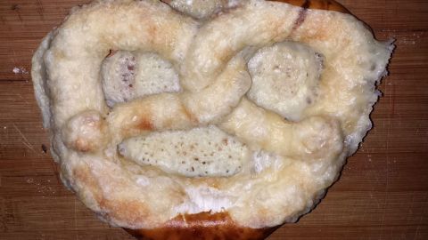 Eine Käsebrezel liegt auf einem Holzbrett, frisch gebacken und mit schmelzendem Käse überzogen, bereit zum Essen.
