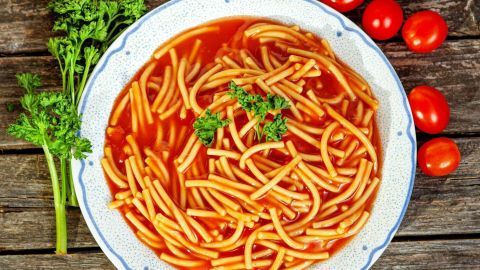 Nudeln in heller Tomatensauce liegen auf einem Teller, umgeben von frischen Tomaten und Kräutern auf rustikalem Holz.