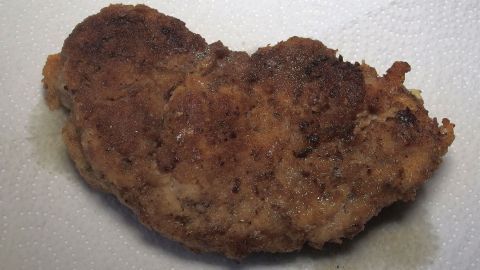 Ein panierter Hähnchenschnitzel liegt auf einer weißen Oberfläche, knusprig und fettreduziert zubereitet.