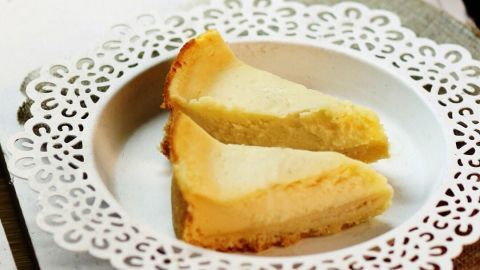 Zwei Stück Käsekuchen liegen auf einem dekorativen Teller, umgeben von einem hellen, rustikalen Tisch.
