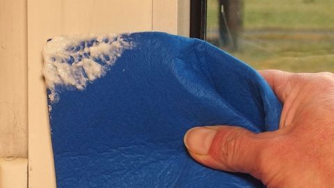 Ein blauer Lappen wird verwendet, um den Fensterrahmen gründlich mit Waschmittel zu reinigen.