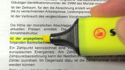 Ein gelber Textmarker hebt wichtige Passagen in einem Vertrag hervor, während eine Hand über den Text führt.