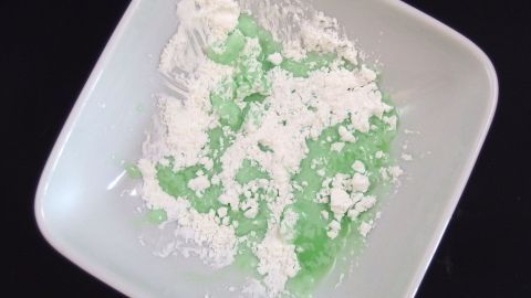 Ein weißer Teller mit grün gefärbtem Zuckerguss und Puderzucker vermischt, in einer neutralen Umgebung.