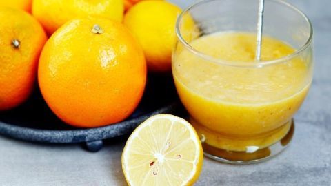 Frische Orangen liegen neben einem Glas Orangenmarmelade, das auf einem Tisch steht und zum Verzehr bereit ist.