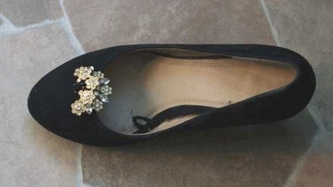 Ein schwarzer Pumps liegt auf einem Steinboden, mit glitzernden Ohrclips, die dekorativ angebracht sind.