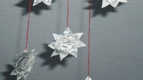Sterne aus leeren Teelichthüllen hängen an Schnüren vor einer grauen Wand und schaffen eine festliche Atmosphäre.