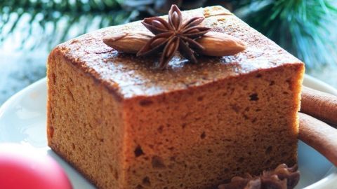 Ein Honigkuchen liegt auf einem weißen Teller, umgeben von weihnachtlicher Dekoration, Kerzenlicht und roten Kugeln.