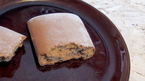Ein Stück Soßenlebkuchen liegt auf einem dunklen Teller und zeigt eine bische abgebissene Kante auf einer natürlichen Oberfläche.