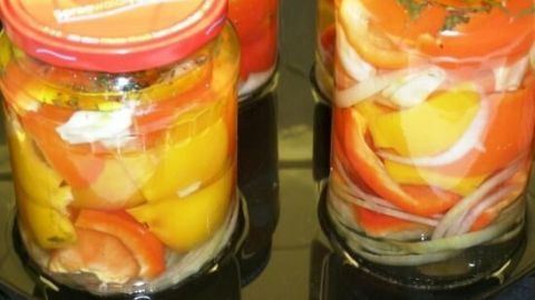 Eingelegte Paprika in Gläsern mit Zwiebeln und Knoblauch stehen auf einem schwarzen Untergrund. Die leuchtenden Farben der Zutaten verleihen dem Bild ein frisches Aussehen.