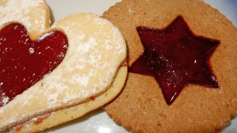 Zwei liebevoll dekorierte Plätzchen liegen auf einem Teller, eines mit Herzform und das andere sternförmig, gefüllt mit Marmelade.