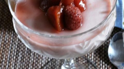 Glasschale mit rosa Creme und Erdbeeren auf einem Tisch mit einem Löffel daneben.