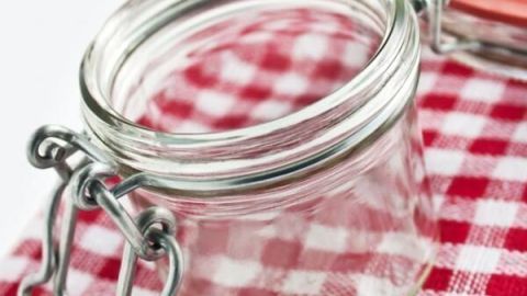 Ein leeres Einmachglas steht offen auf einer rot-weiß karierten Tischdecke.