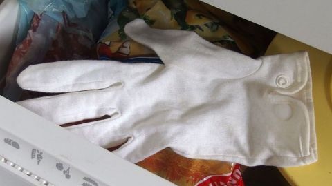 Ein weißer Handschuh liegt auf einem gelben Untergrund in einer Schublade, um den festen Ring zu lösen.
