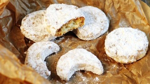 Ausstechplätzchen liegen auf braunem Papier, einige sind mit Puderzucker bestäubt, und einer ist halb aufgegessen.