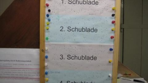 Ein Schild mit Listen zum Einräumen eines Gefrierschranks, unterteilt in "1. Schublade" bis "4. Schublade", hängt an der Wand.