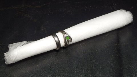 Auf einem schwarzen Untergrund liegen mehrere Ringe um eine zusammengerollte, weiße Serviette, die sanft aufbewahrt wird.