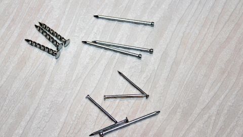 Schrauben und Nägel liegen verstreut auf einem hellen Holzuntergrund, bereit für die Verwendung zur Löchern in Tapeten vorbeugen.