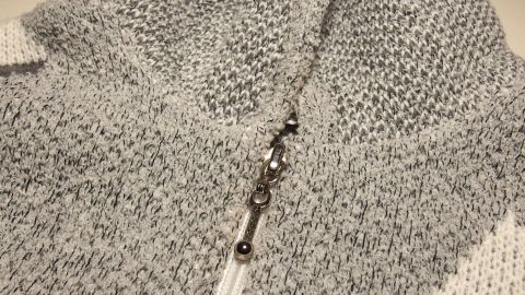 Ein grauer Strickpullover mit Reißverschluss liegt flach auf einem Tisch, der Reißverschluss ist geöffnet und gut sichtbar.