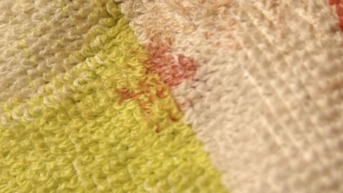 Ein Textil zeigt einen kleinen Blutfleck, der auf einer bunten, strukturierten Oberfläche sichtbar ist.