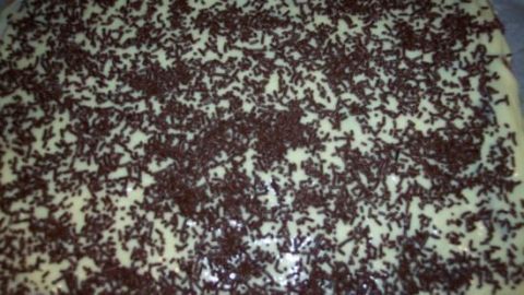 Eine glänzende Schokoglasur bedeckt einen kuchenartigen Untergrund, der mit Schokoladenstreuseln dekoriert ist.
