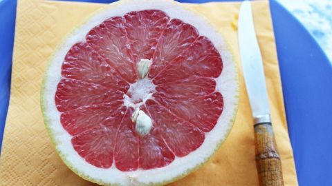 Eine halbierte Grapefruit liegt auf einem gelben Serviette, daneben ein Messer; sie wird für das Kauen und Ausspucken zubereitet.