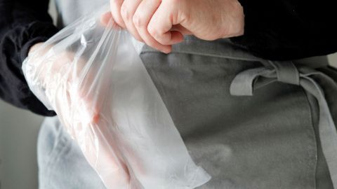 Eine Hand zieht sich einen durchsichtigen Einweghandschuh über, während sie eine Schürze trägt, um beim Kuchenbacken sauber zu bleiben.
