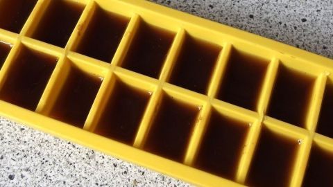 Gelbe Silikonform mit runden Fächern, gefüllt mit Obstwasser aus Konservendosen, auf einer grauen Arbeitsfläche.